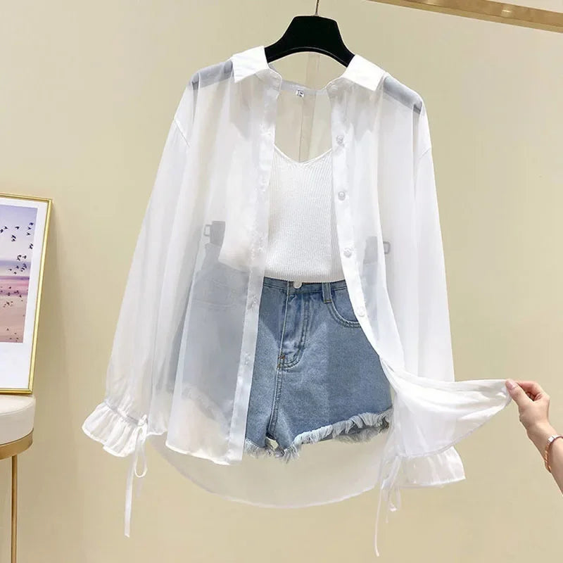 White sheer blouse with denim shorts on a hanger against a beige wall.