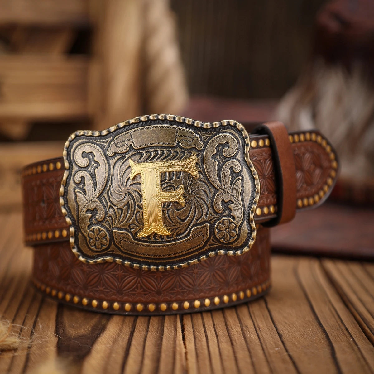 Brown leather belt with a gold and silver buckle on a wooden surface