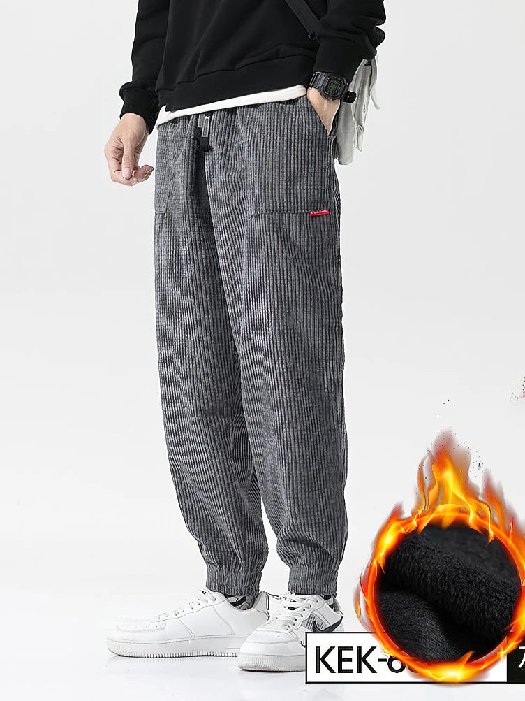 Person wearing gray corduroy pants with a flame graphic and 'KEK' branding on a white background. Men's baggy corduroy jogger pants, tech fleece sweatpants, autumn winter harem trousers, elastic waist, thermal, UK FTF Market.