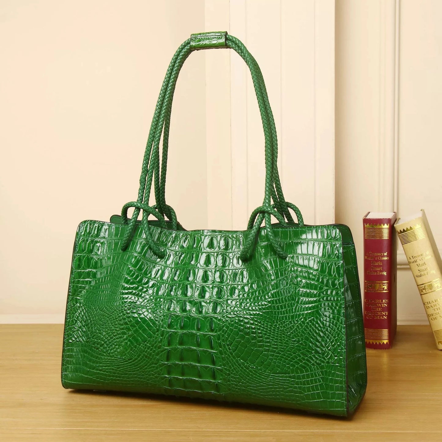 Green textured handbag on a wooden surface with books in the background. Luxury women’s tote bag in genuine red crocodile leather. Large capacity, stylish handle, fashion travel handbag. Perfect for shoulder or portable use UK.