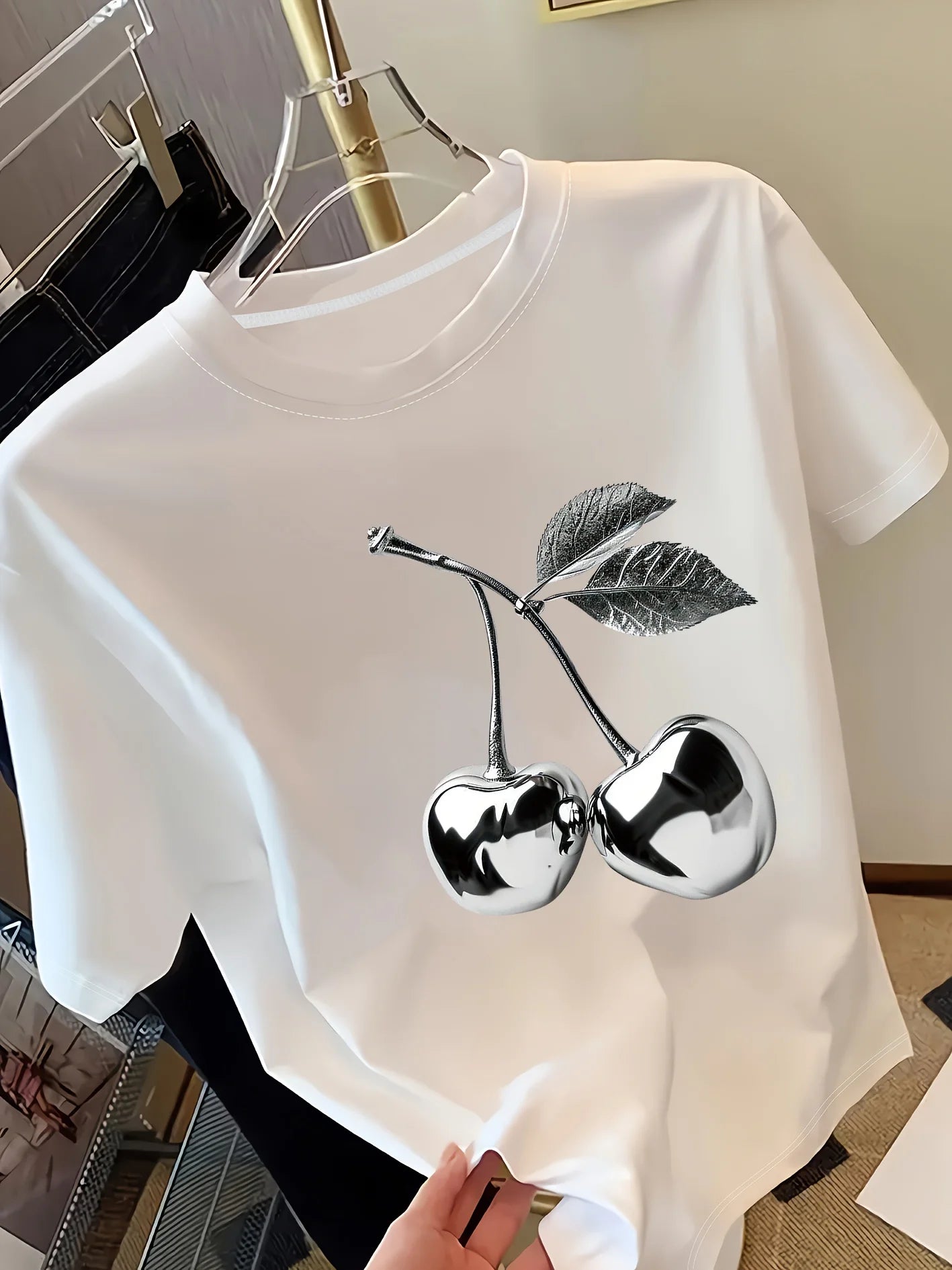 White t-shirt with silver cherry design on a hanger.