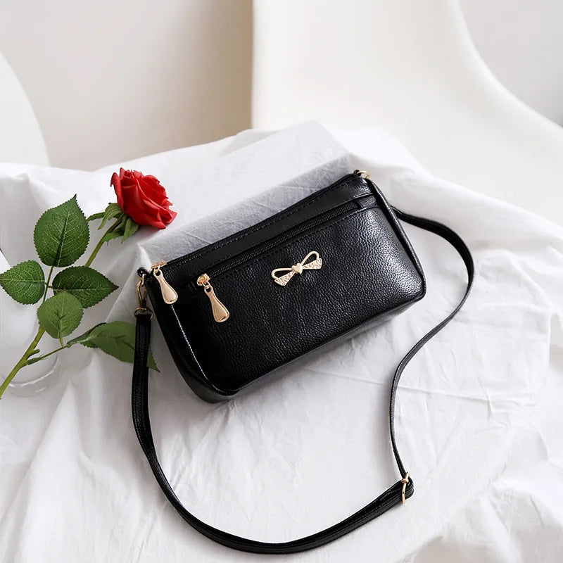 Black handbag with a gold bow detail on a white surface with a red rose.