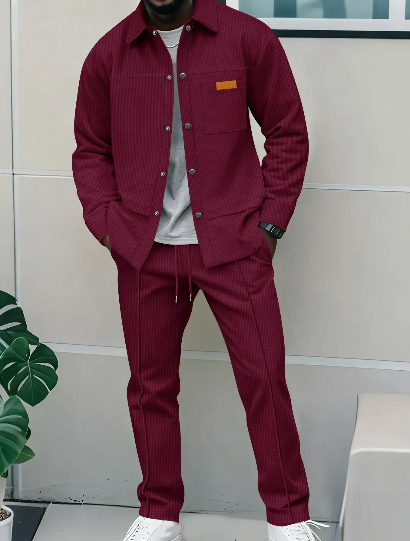 Person wearing a burgundy jacket and pants with a white shirt underneath, standing against a light-colored wall.