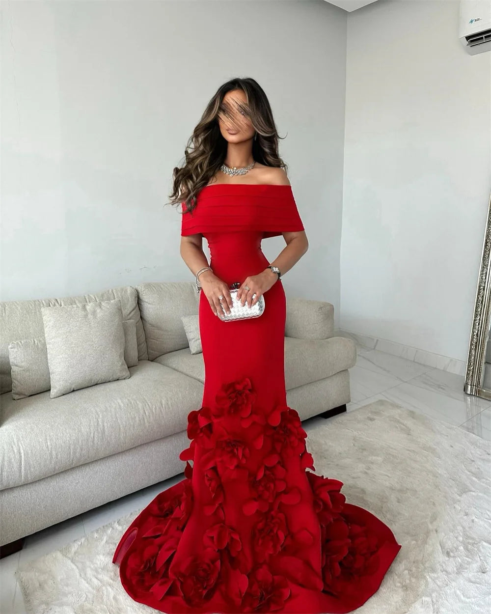 Woman in a red off-shoulder gown with floral details standing in a living room.