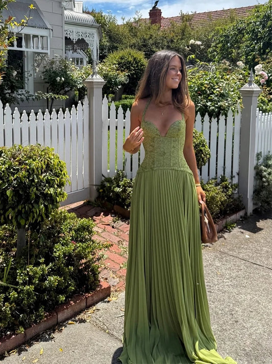 Woman in a green dress standing in a garden with a white picket fence.
