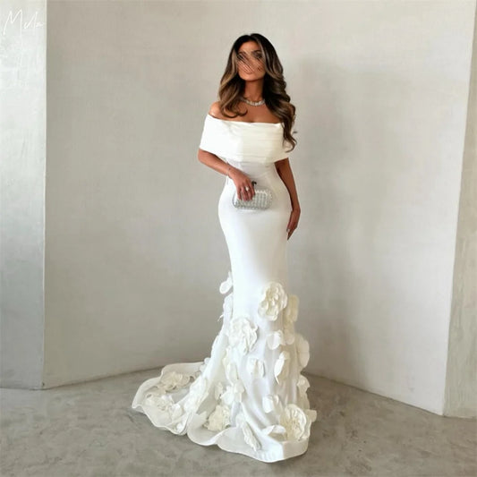 Woman wearing a white off-shoulder gown with floral details against a plain background