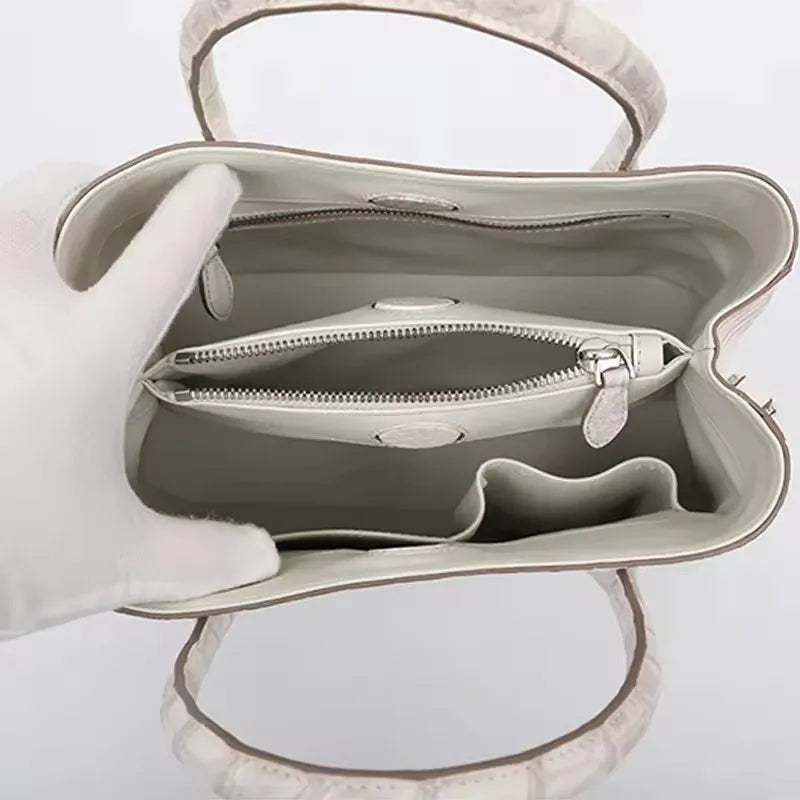 Open beige handbag with a zipper on a light gray background. Genuine crocodile leather tote bag for women, waterproof pillow shape with zipper closure and removable strap. Luxury high-quality fashion accessory.