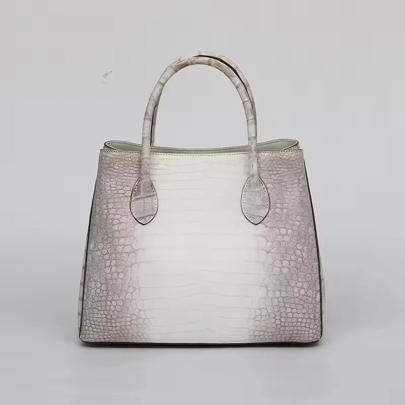 Handbag with crocodile texture on a light gray background. Genuine crocodile leather tote bag for women, waterproof pillow shape with zipper closure and removable strap. Luxury high-quality fashion accessory.