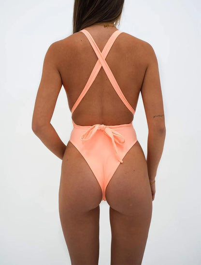 Person wearing a peach-colored swimsuit with criss-cross straps on a white background. Solid pink high cut v-neck monokini with lace-up detail, adjustable straps, beachwear for women, true to size, flattering, UK swim style.