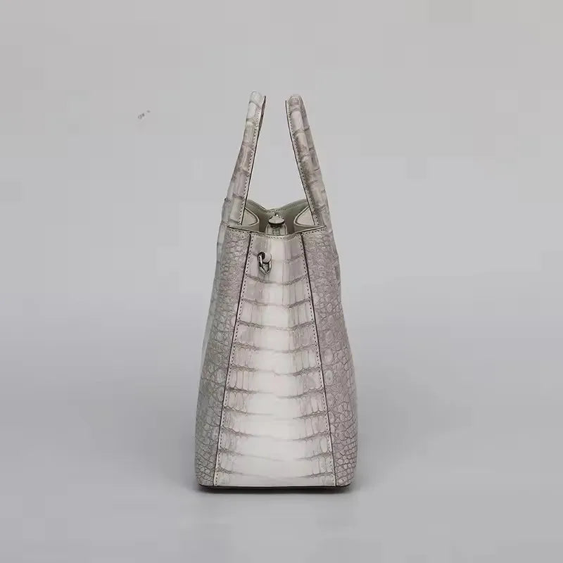 Light gray textured handbag on a light gray background. Genuine crocodile leather tote bag for women, waterproof pillow shape with zipper closure and removable strap. Luxury high-quality fashion accessory.