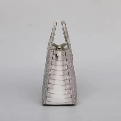 Light gray textured handbag on a light gray background. Genuine crocodile leather tote bag for women, waterproof pillow shape with zipper closure and removable strap. Luxury high-quality fashion accessory.