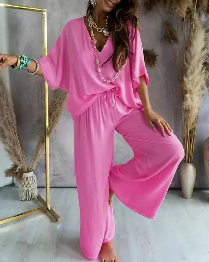 Woman wearing a pink outfit with a necklace, standing in a room with decorative elements.
