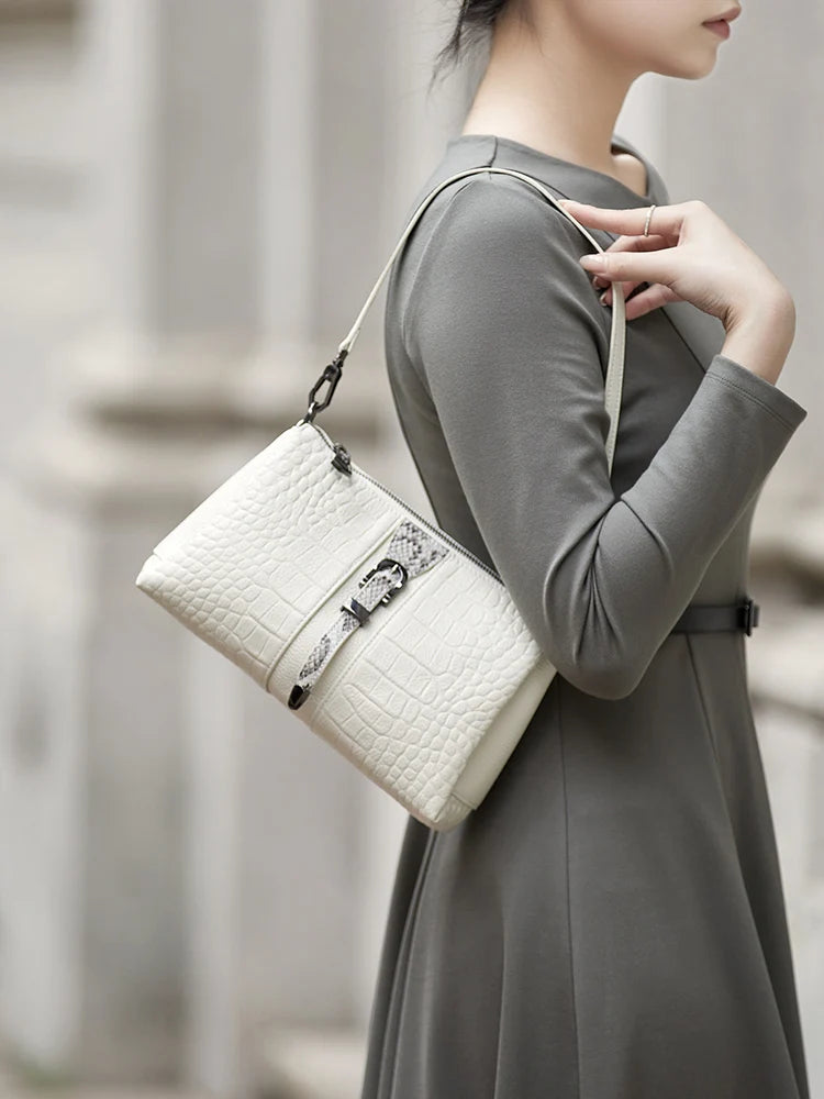 Woman holding a white handbag with a blurred architectural background. Genuine leather women’s shoulder messenger bag in black and gray. Soft cow leather, flap style with zipper closure. Perfect versatile bag for all seasons. 