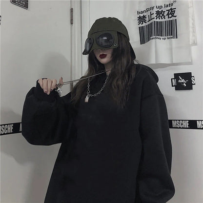 Person wearing a black hoodie and cap with goggles, standing against a white wall with text and logos.