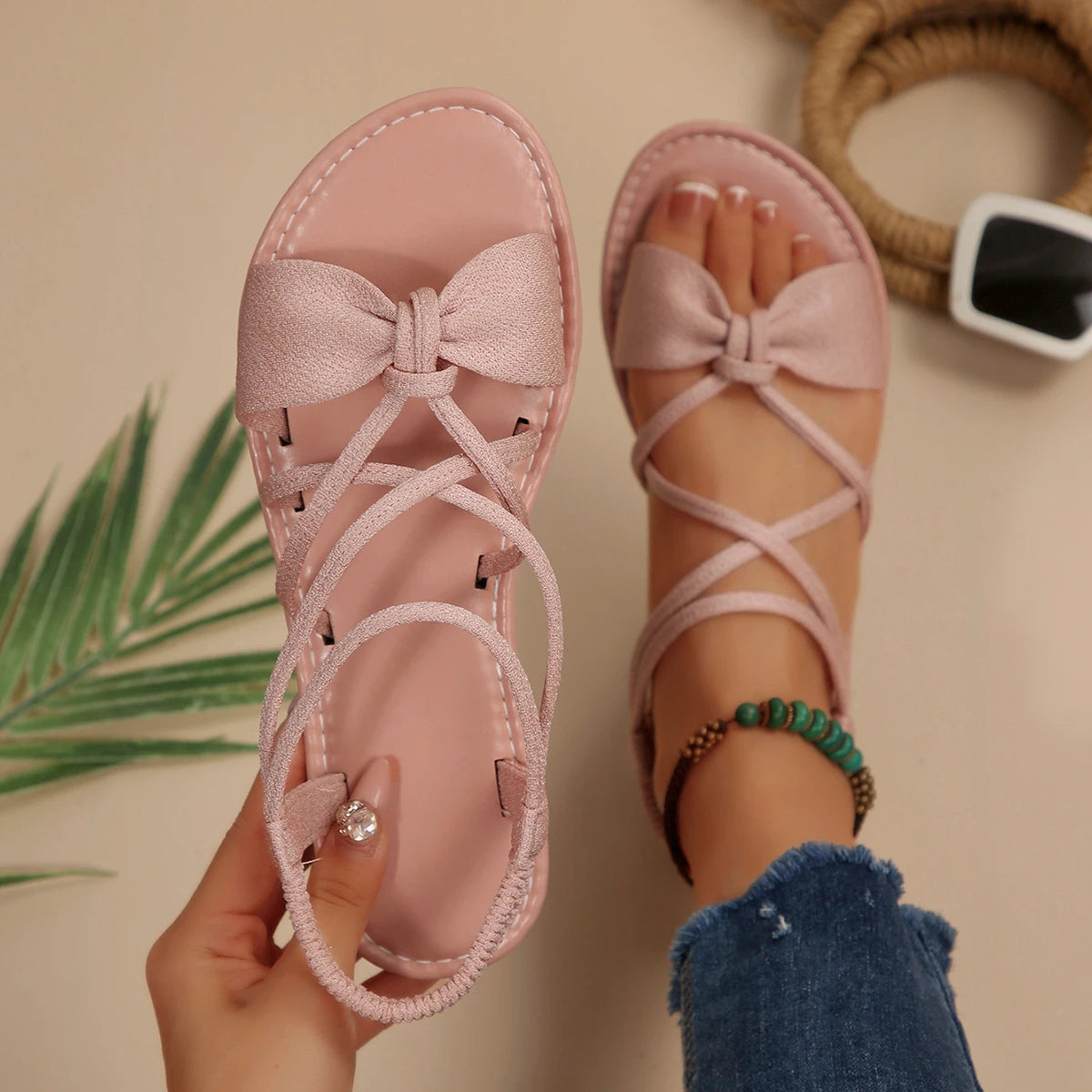 Pink sandals with bow details held by a person, with a plant in the background.