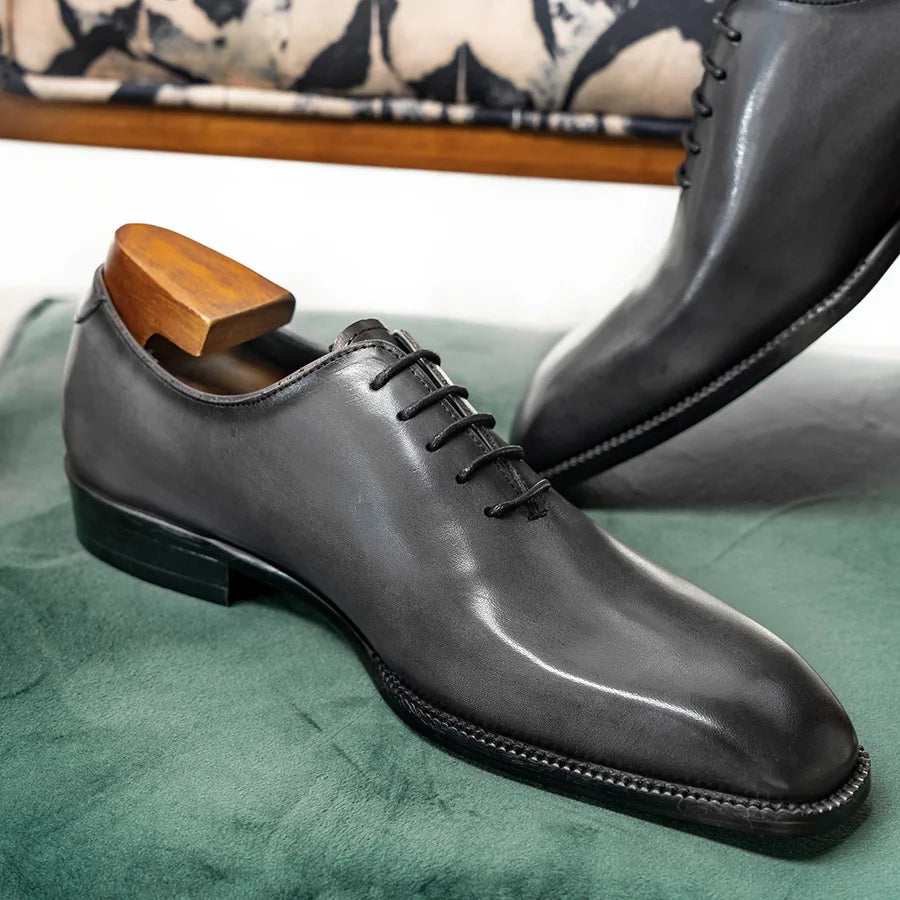 Black leather dress shoe with wooden shoe horn on a green surface