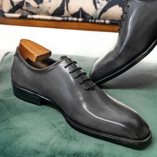 Black leather dress shoe with wooden shoe horn on a green surface