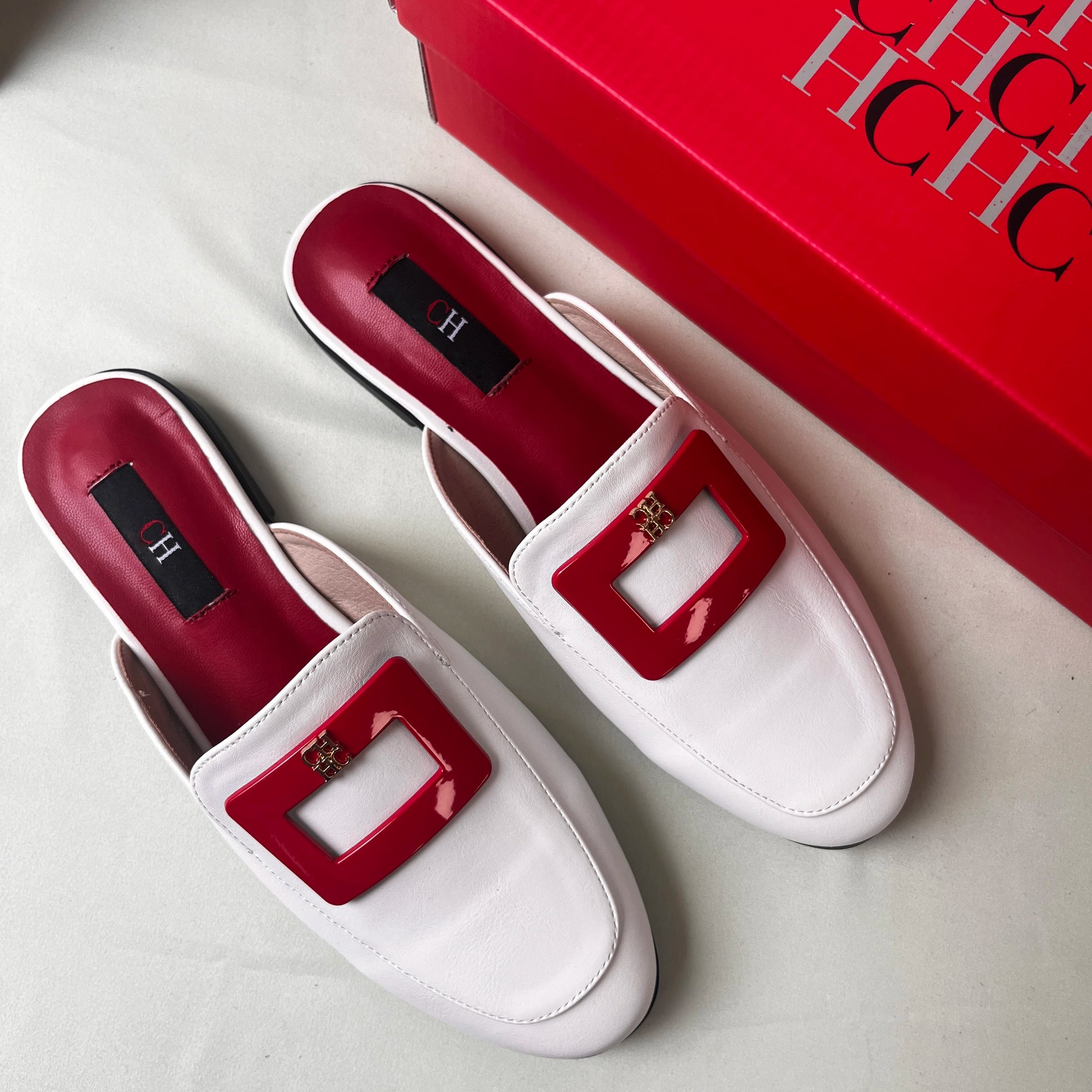 White loafers with red square buckles next to a red box with 'H' branding.