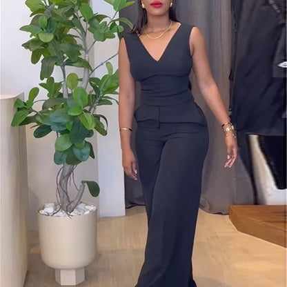 Woman in a dark gray jumpsuit standing indoors with a plant and furniture in the background. Women’s striped print blouse and elastic waist pants two-piece suit. Sleek, comfortable, breathable office wear perfect for spring and summer.