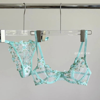 Teal floral lingerie set hanging on a rack against a gray background