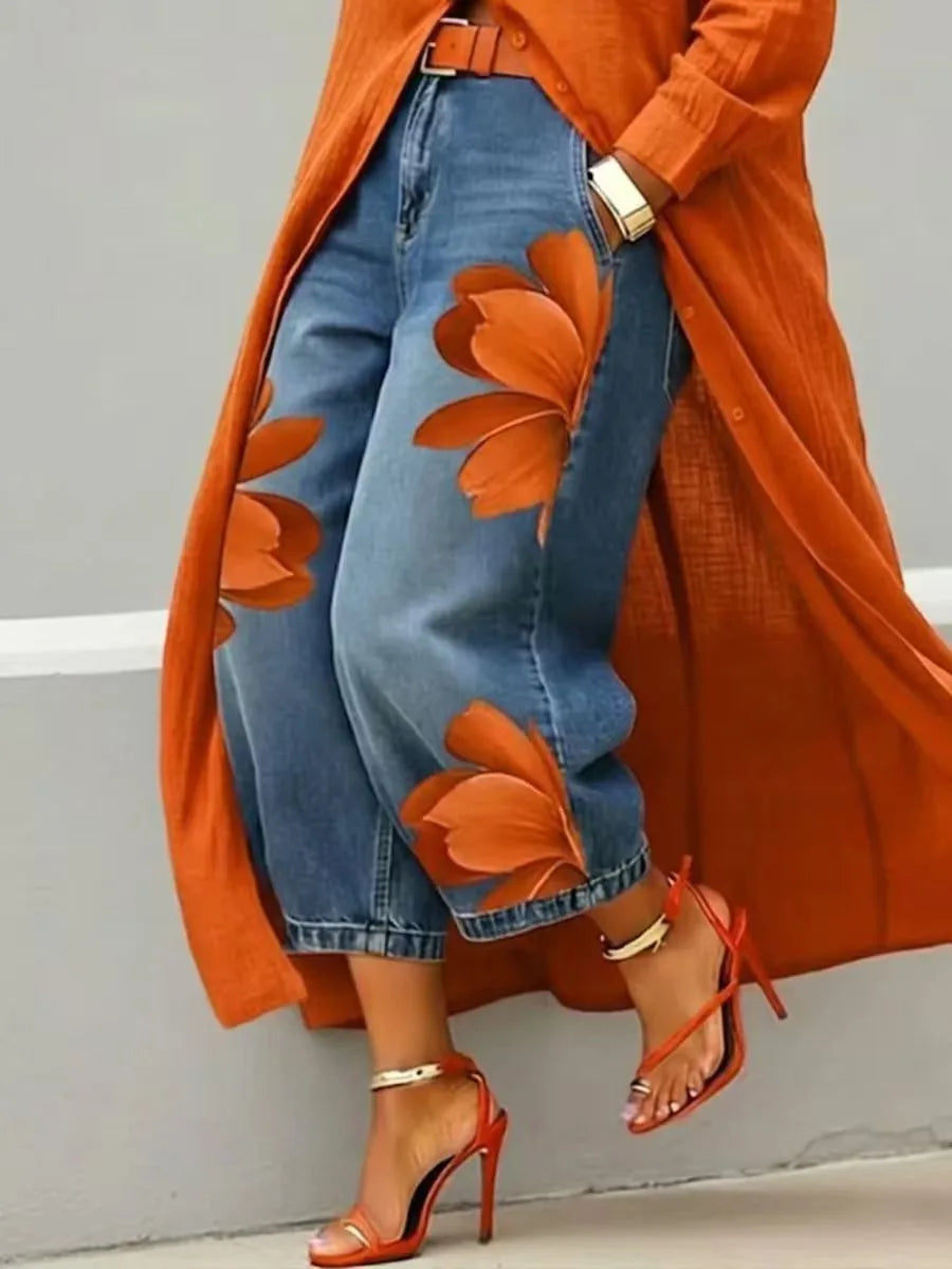 Person wearing an orange floral-patterned coat, blue jeans, and red high-heeled shoes against a gray background.