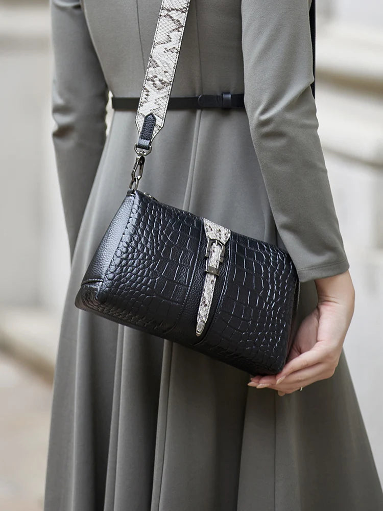 Person holding a black crocodile-patterned handbag with a snake skin strap . Genuine leather women’s shoulder messenger bag in black and gray. Soft cow leather, flap style with zipper closure. Perfect versatile bag for all seasons.