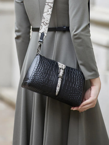 Person holding a black crocodile-patterned handbag with a snake skin strap . Genuine leather women’s shoulder messenger bag in black and gray. Soft cow leather, flap style with zipper closure. Perfect versatile bag for all seasons.
