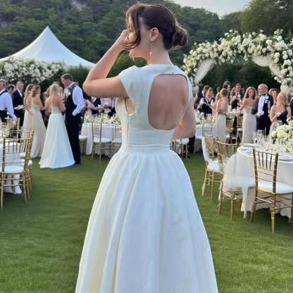 Woman in a white dress at an outdoor wedding reception with guests and decorations.