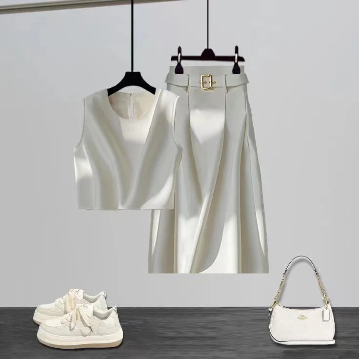 White sleeveless top, pants, sneakers, and handbag on a gray surface with a white background. Women’s high-end two-piece set with sleeveless O-neck crop top and mid-calf A-line skirt. Elegant, minimalist office suit, beaded detail, UK fashion.