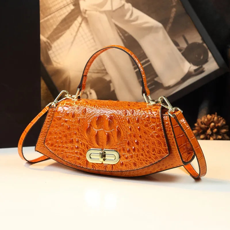 Brown crocodile skin handbag with gold clasp on a white surface, blurred background