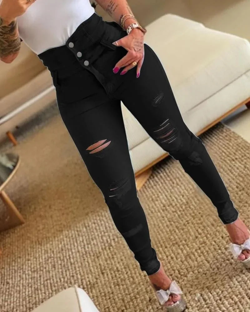 Person wearing black distressed jeans in a casual indoor setting. Women’s slim pencil jeans, high waist bodycon fit. Casual sheath denim trousers with button detail, ankle length. Trendy Y2K style UK.