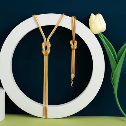 Gold necklaces on a white circular stand with a white tulip on a dark background. Women’s vintage goth snake twisted chain necklace & bracelet set with tassel, Y2K style jewelry accessories for fashion-forward looks.