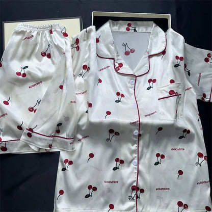 White pajama set with red cherry pattern on a dark background. Women’s cherries print summer pajamas set—faux satin V-neck top and shorts, funny cute style. Lightweight, comfortable, UK fashion set.