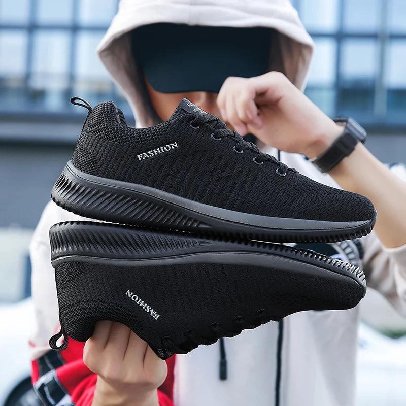 Black sneakers held by a person with a blurred background. Men’s breathable running sneakers with mesh lining, PU insole, EVA outsole, lightweight casual sports shoes, perfect for jogging and walking.