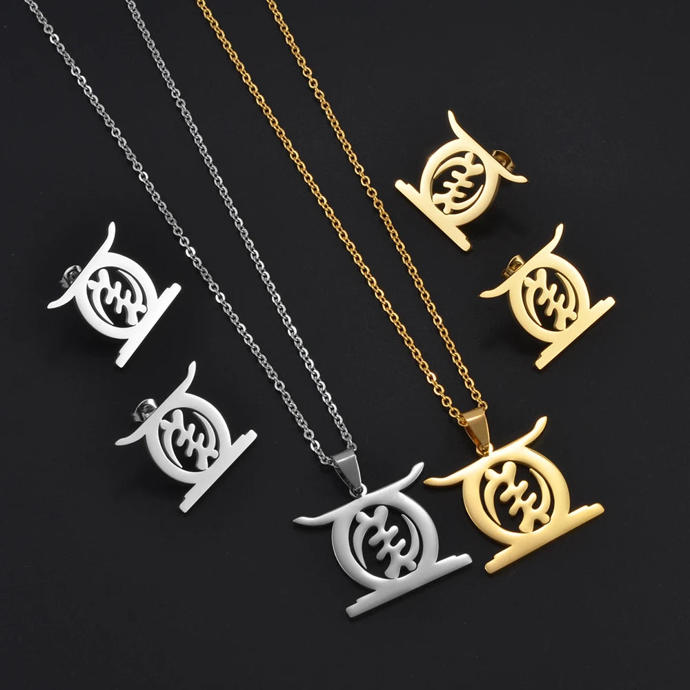 African Gye Stool pendant necklace and stud earrings set in gold and silver flat lay on dark fabric