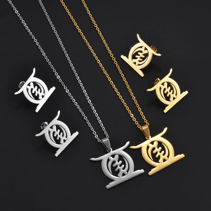 African Gye Stool pendant necklace and stud earrings set in gold and silver flat lay on dark fabric