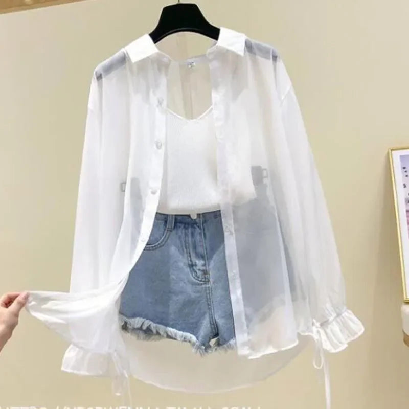 White sheer blouse over a white shirt and denim shorts on a hanger against a beige wall.