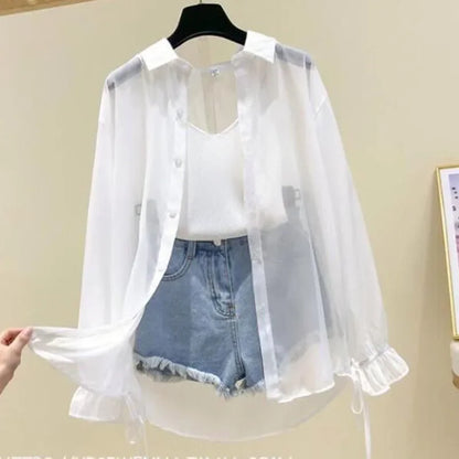White sheer blouse over a white shirt and denim shorts on a hanger against a beige wall.