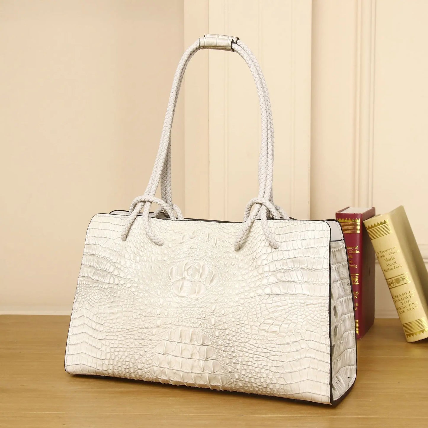 White textured handbag on a wooden surface with books in the background. Luxury women’s tote bag in genuine red crocodile leather. Large capacity, stylish handle, fashion travel handbag. Perfect for shoulder or portable use UK.