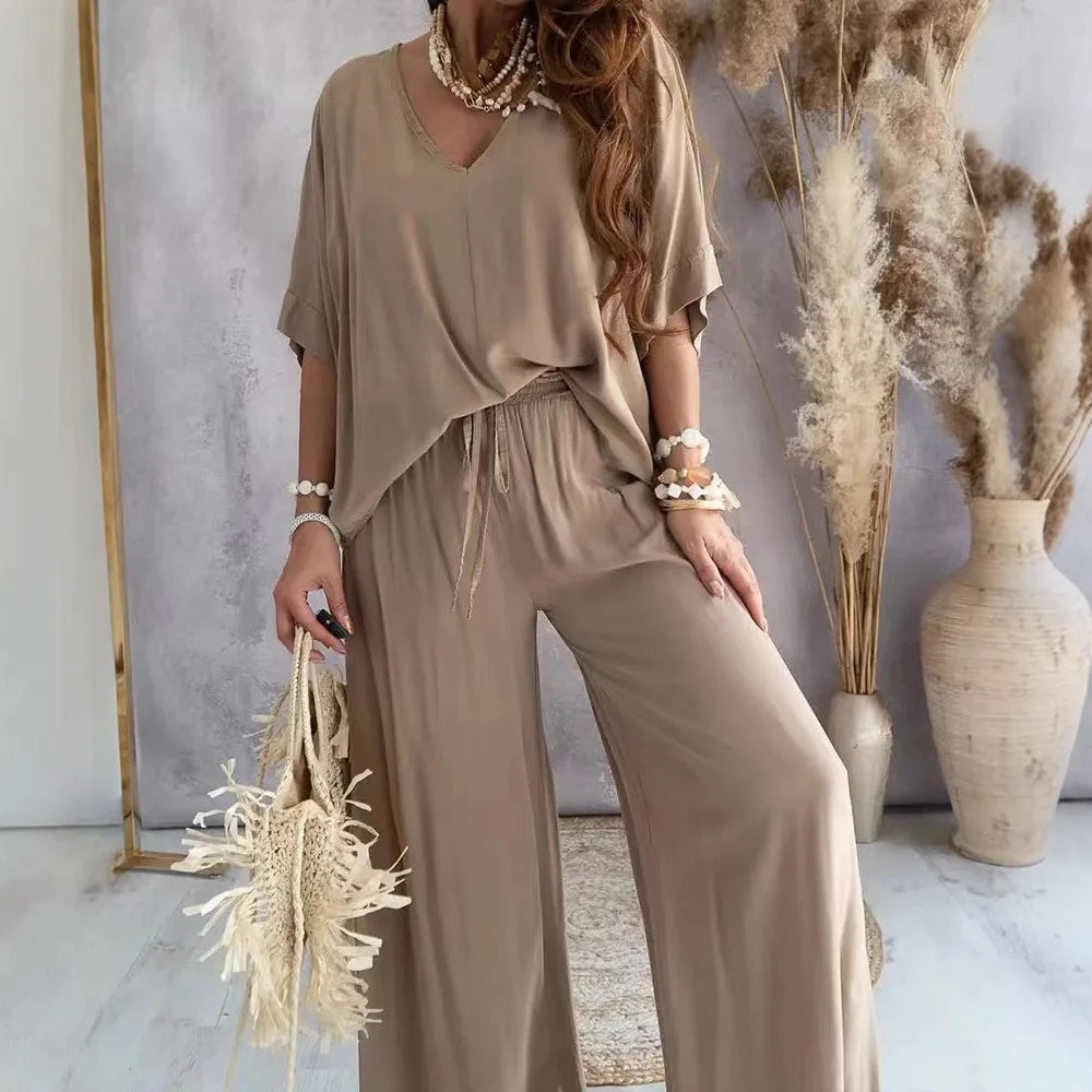 Woman in a beige outfit standing in a room with decorative plants and vases.