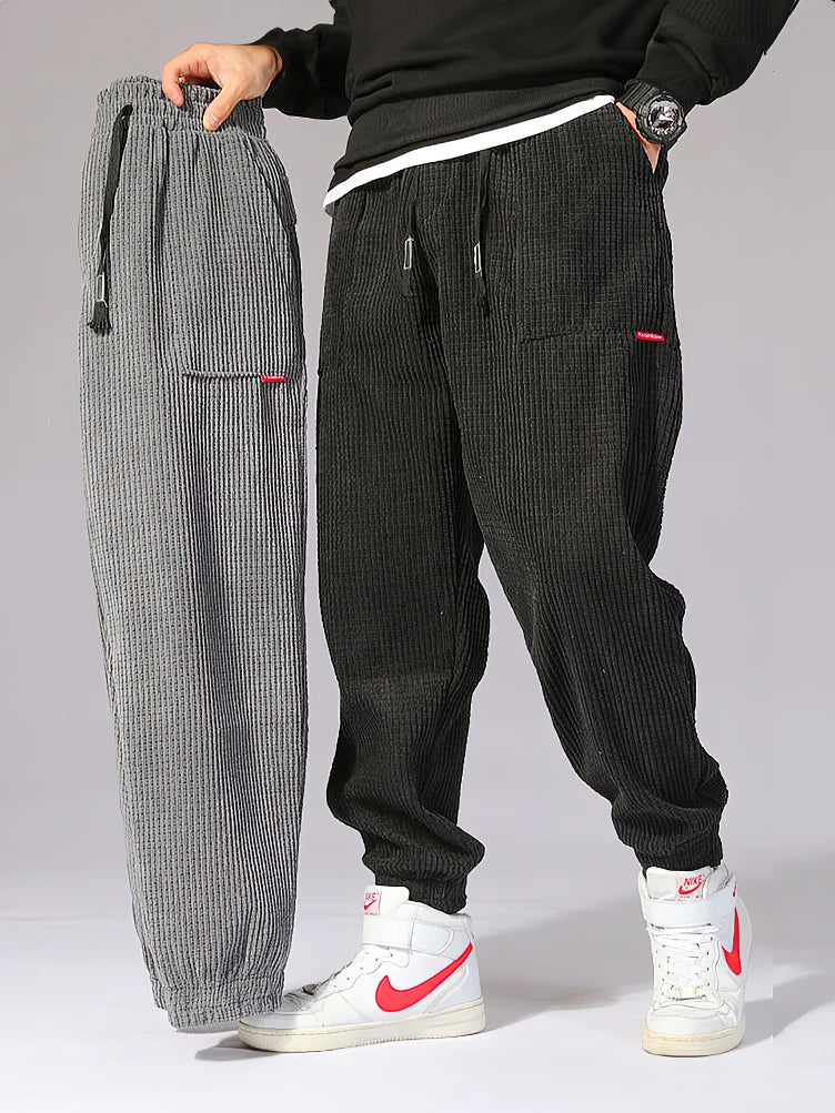 Two pairs of corduroy pants, one gray and one black, displayed side by side on a neutral background. Men's baggy corduroy jogger pants, tech fleece sweatpants, autumn winter harem trousers, elastic waist, thermal, UK FTF Market.