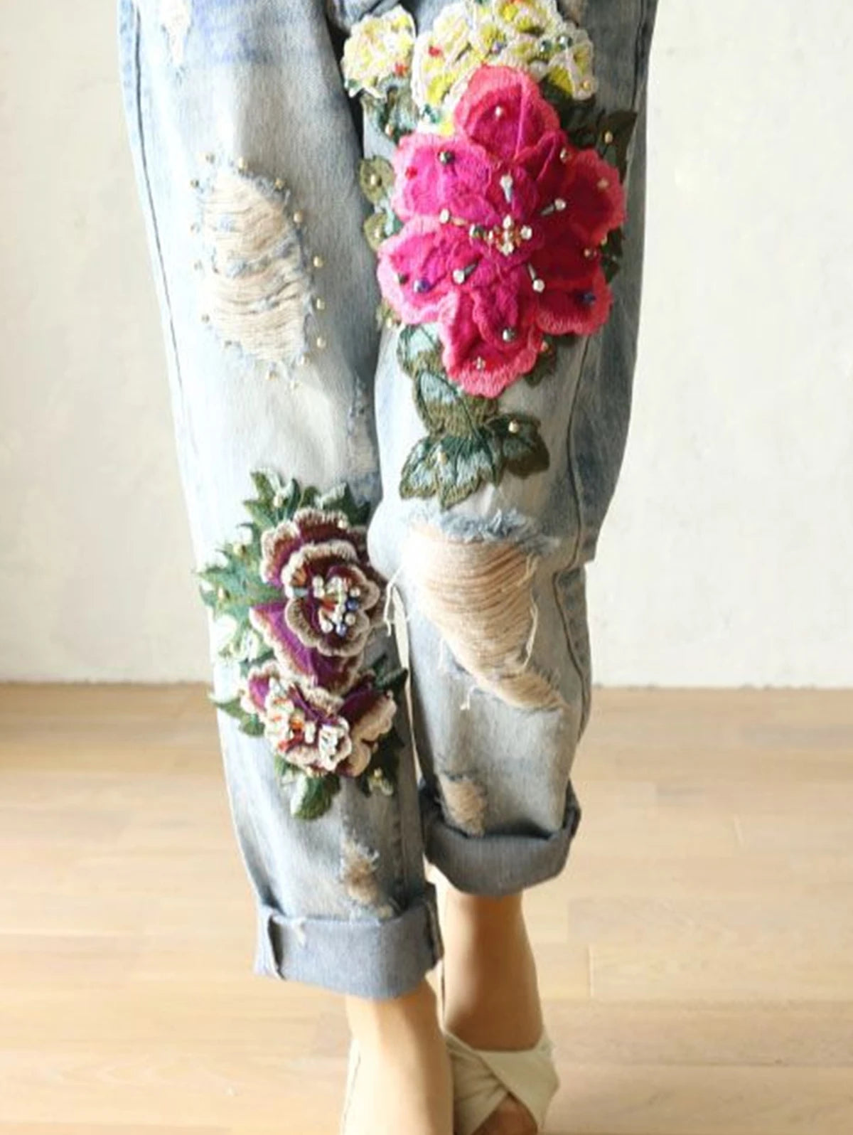 Gray pants with floral and leaf patterns on a wooden floor. Floral embroidered harem jeans for women. Loose, high waist, elegant denim trousers. Vintage Y2K style. UK online store.