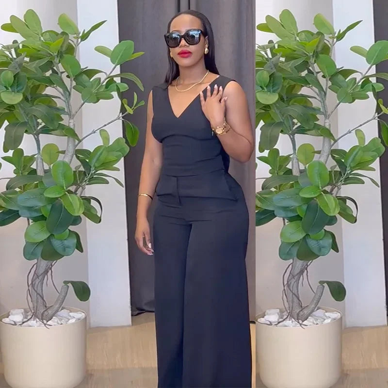 Woman in a black outfit standing between two potted plants indoors. Women’s striped print blouse and elastic waist pants two-piece suit. Sleek, comfortable, breathable office wear perfect for spring and summer.