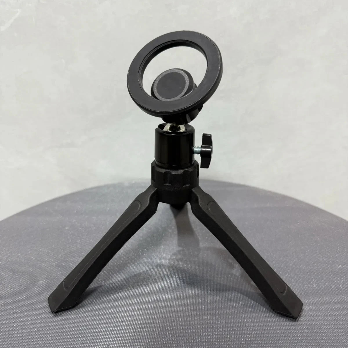 Black microphone stand with circular mount on a gray surface. Magnetic phone tripod and wireless grip with remote control. Fits iPhone MagSafe and Samsung devices. Lightweight selfie stick tripod for creators.