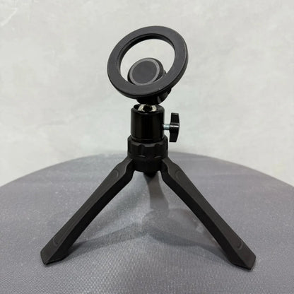 Black microphone stand with circular mount on a gray surface. Magnetic phone tripod and wireless grip with remote control. Fits iPhone MagSafe and Samsung devices. Lightweight selfie stick tripod for creators.