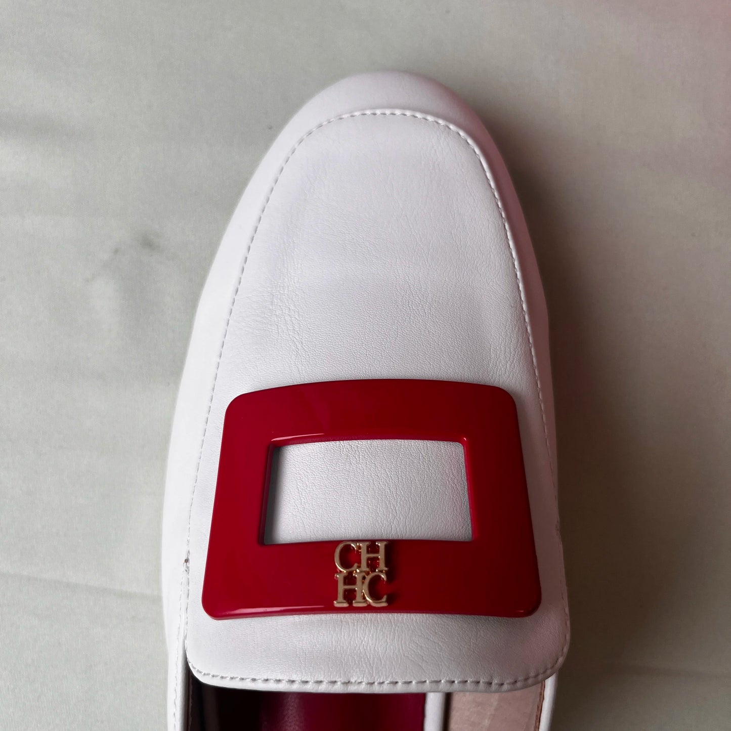 White loafer with a red buckle on a light gray background