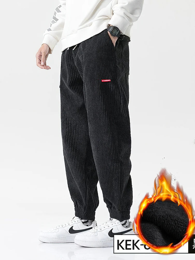 Person wearing black corduroy pants with a flame graphic and 'KEK' text on a white background. Men's baggy corduroy jogger pants, tech fleece sweatpants, autumn winter harem trousers, elastic waist, thermal, UK FTF Market.