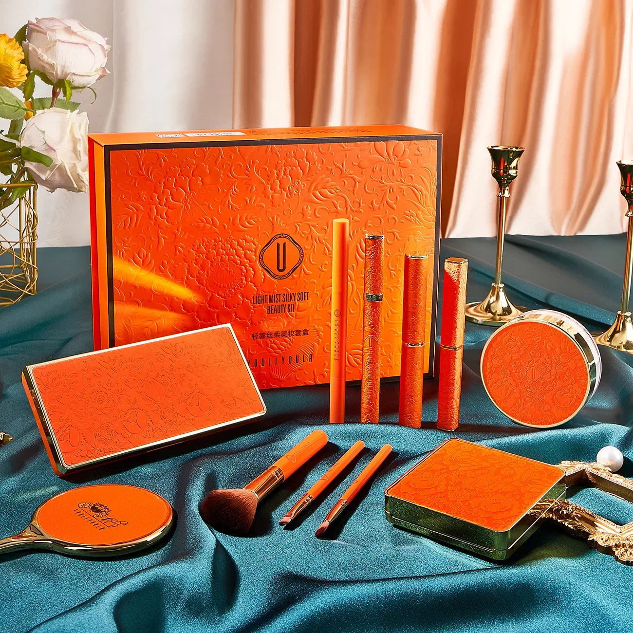Orange cosmetic set with tools on a blue fabric background. Christmas makeup gift box with BB cream, lipstick, eyeshadow, eyebrow pencil, and brushes. Holiday beauty set for women & girls.