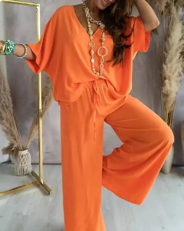Person wearing an orange outfit with a necklace, standing against a neutral background.