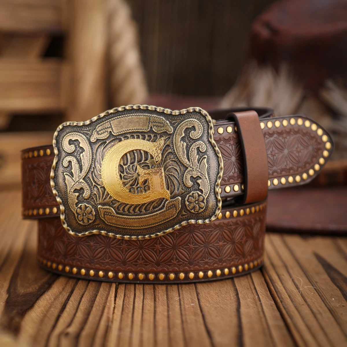 Brown leather belt with a gold and silver buckle on a wooden surface